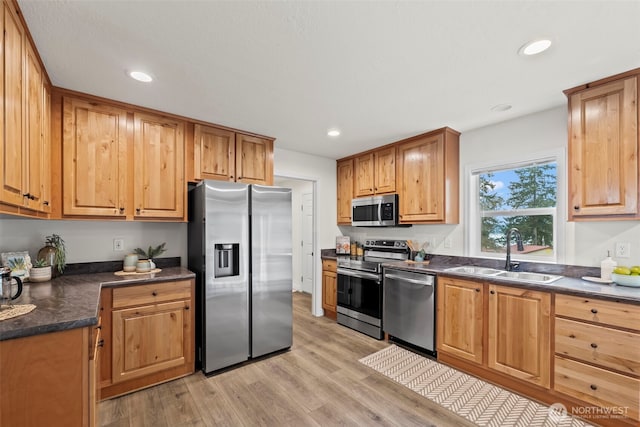 kitchen featuring a sink, stainless steel appliances, light wood-type flooring, and dark countertops