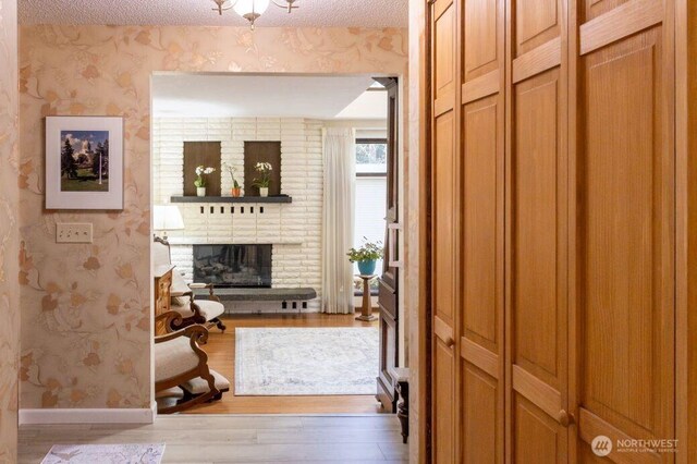 corridor with a textured ceiling, wallpapered walls, baseboards, and wood finished floors