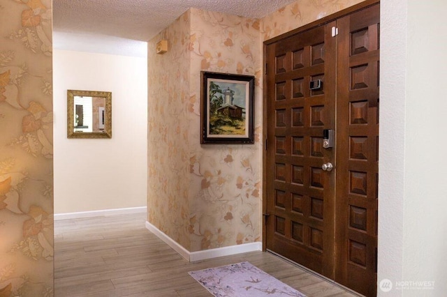 foyer featuring a textured ceiling, wood finished floors, and wallpapered walls