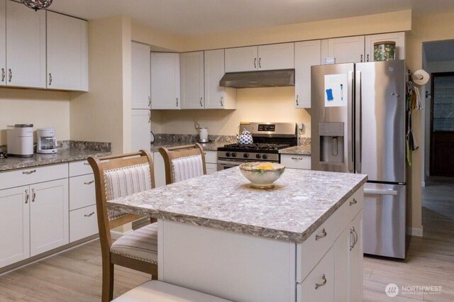 kitchen with stainless steel appliances, under cabinet range hood, white cabinetry, light wood-type flooring, and a center island