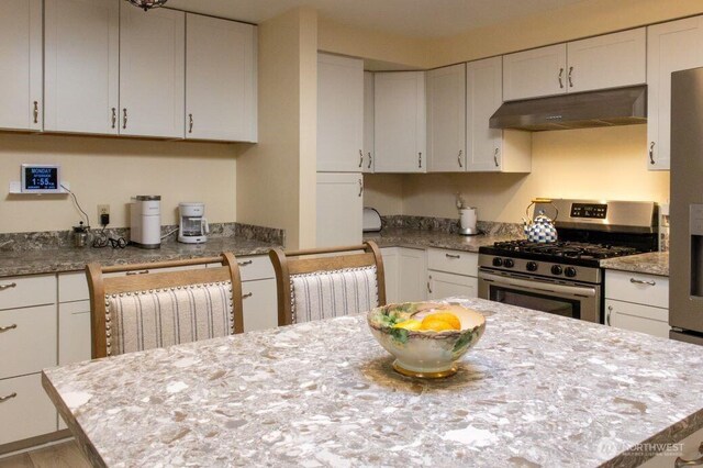 kitchen featuring under cabinet range hood, stainless steel range with gas stovetop, and white cabinets