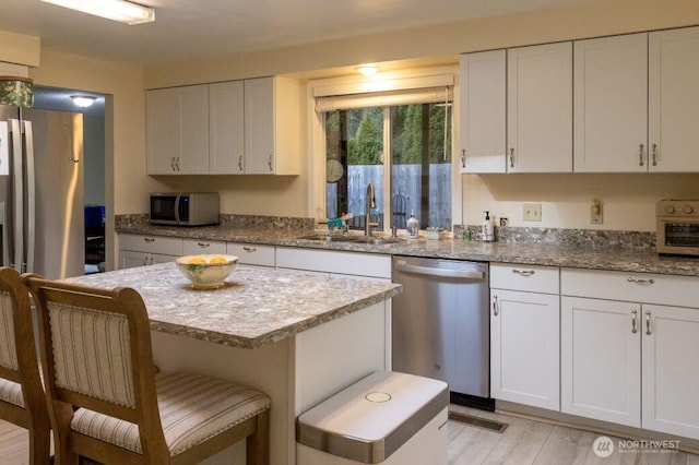 kitchen featuring a sink, stainless steel appliances, a breakfast bar, and white cabinetry