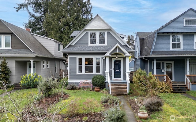 view of front of house featuring covered porch, a front yard, and a shingled roof