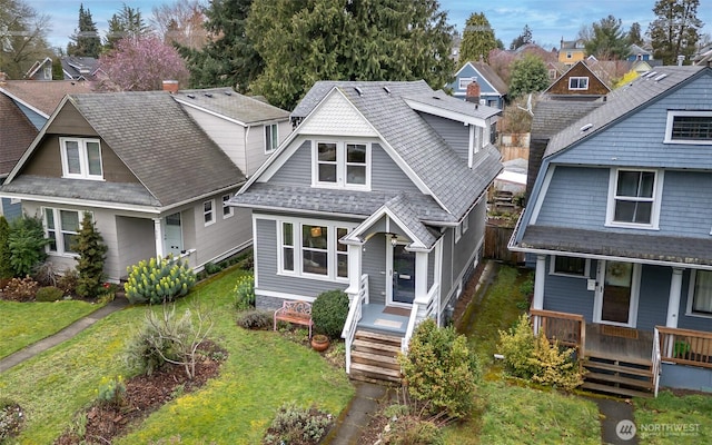 view of front of home with a residential view, covered porch, a front lawn, and a shingled roof