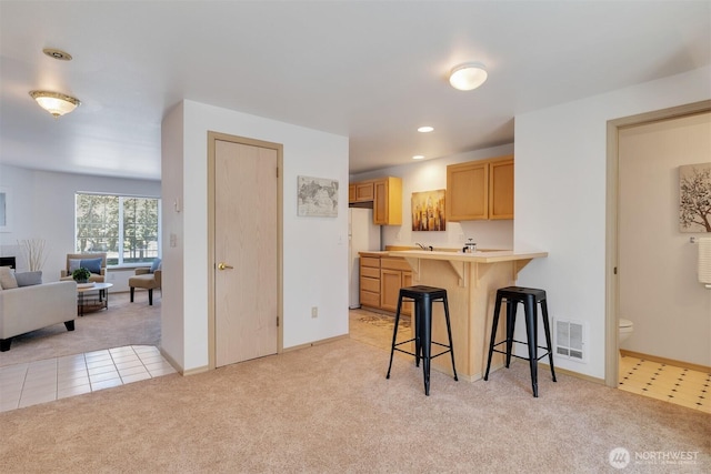 kitchen with visible vents, light colored carpet, a breakfast bar area, light countertops, and freestanding refrigerator