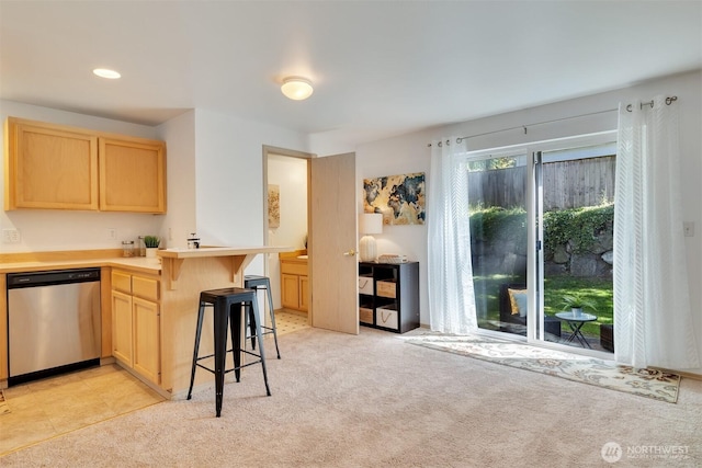 kitchen featuring light colored carpet, a kitchen breakfast bar, stainless steel dishwasher, and light brown cabinetry