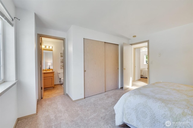 bedroom with connected bathroom, baseboards, light colored carpet, a closet, and a sink