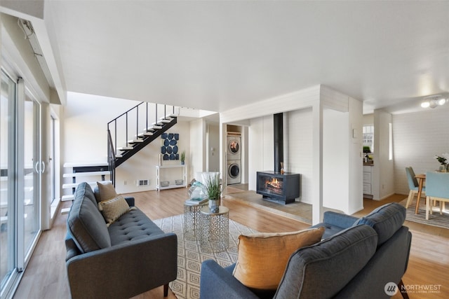 living room featuring visible vents, stairway, stacked washer and clothes dryer, and light wood finished floors