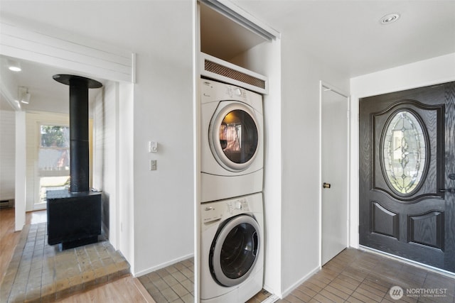 laundry room featuring laundry area, stacked washer / dryer, wood finished floors, and a wood stove