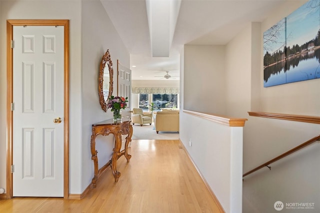 corridor with an upstairs landing, baseboards, and light wood finished floors