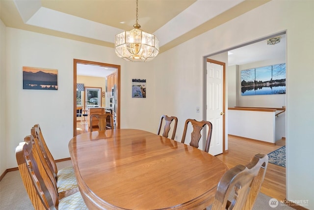 dining area with baseboards, light wood finished floors, a raised ceiling, and an inviting chandelier