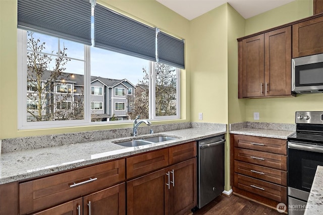 kitchen featuring a sink, stainless steel appliances, light stone countertops, and dark wood-style flooring