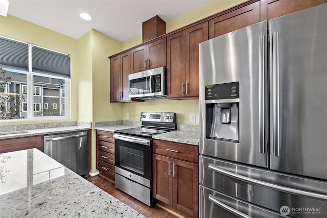 kitchen with dark wood-type flooring, light stone counters, recessed lighting, and appliances with stainless steel finishes