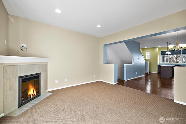 unfurnished living room featuring baseboards, carpet flooring, recessed lighting, a fireplace, and a notable chandelier