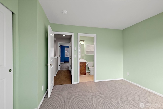 unfurnished bedroom featuring ensuite bath, light colored carpet, and baseboards