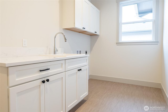 washroom featuring cabinet space, hookup for a washing machine, baseboards, and a sink