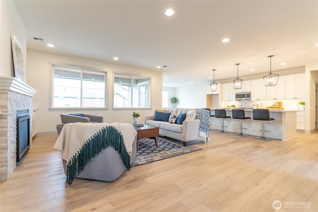 living room with recessed lighting, visible vents, light wood-style floors, and a glass covered fireplace