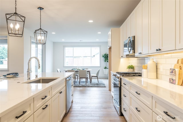 kitchen with decorative backsplash, light wood-style flooring, appliances with stainless steel finishes, white cabinets, and a sink