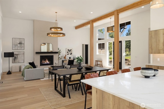 dining room featuring a warm lit fireplace, light wood-type flooring, a towering ceiling, and recessed lighting