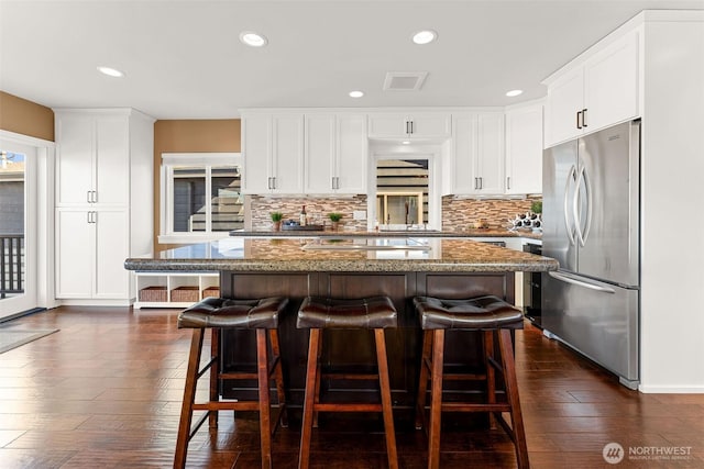 kitchen featuring visible vents, backsplash, a breakfast bar area, stainless steel refrigerator, and dark wood-style flooring