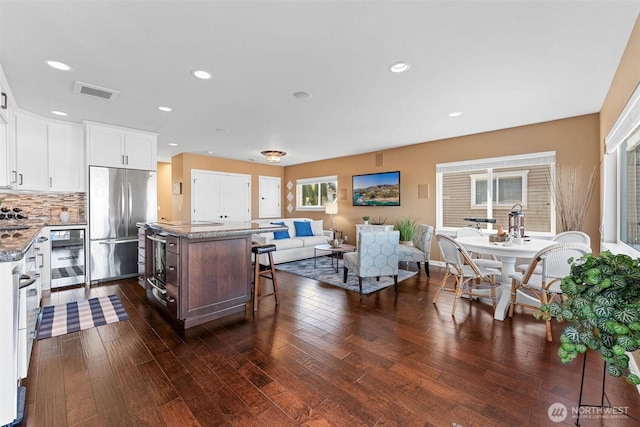 kitchen with dark wood finished floors, visible vents, a center island, and stainless steel built in fridge