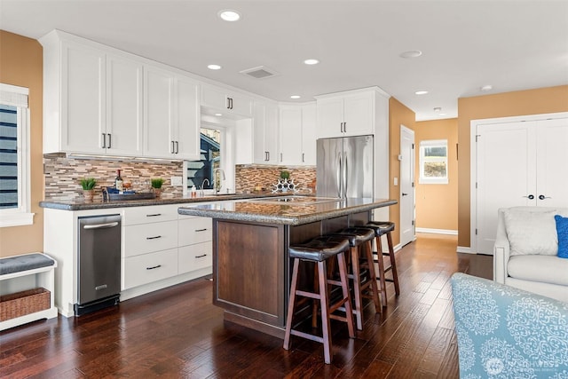 kitchen with visible vents, a breakfast bar, dark wood-type flooring, stainless steel fridge, and a center island