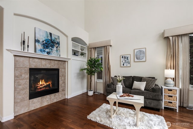 living room featuring built in features, a fireplace, baseboards, and wood finished floors