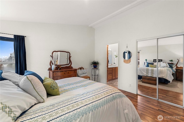 bedroom featuring ensuite bathroom, wood finished floors, a closet, baseboards, and lofted ceiling