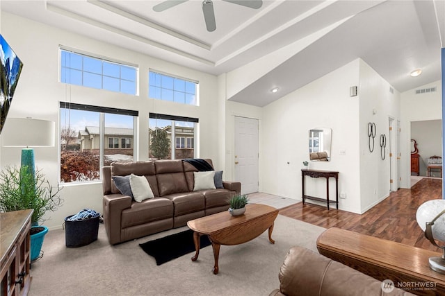 living room featuring a tray ceiling, wood finished floors, a ceiling fan, and visible vents