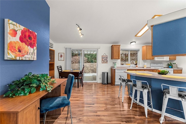 kitchen featuring white appliances, a breakfast bar, a sink, light countertops, and light wood-style floors