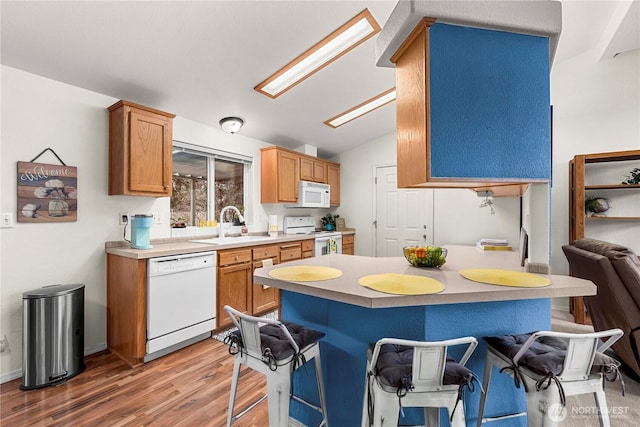 kitchen featuring lofted ceiling with skylight, a breakfast bar, a sink, white appliances, and light wood finished floors