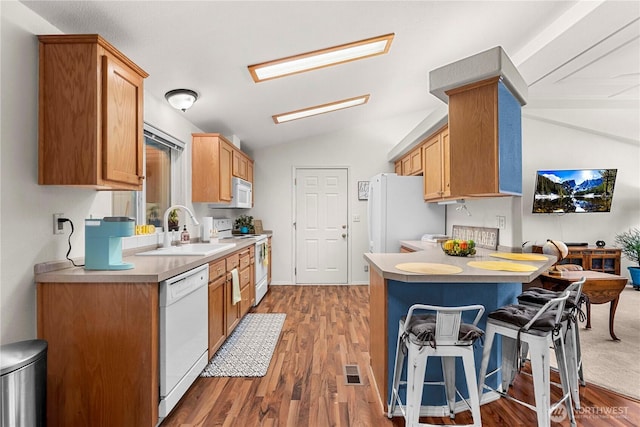 kitchen with white appliances, a breakfast bar area, a peninsula, a sink, and vaulted ceiling