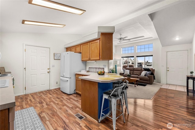 kitchen with a kitchen bar, a peninsula, light wood-type flooring, and freestanding refrigerator