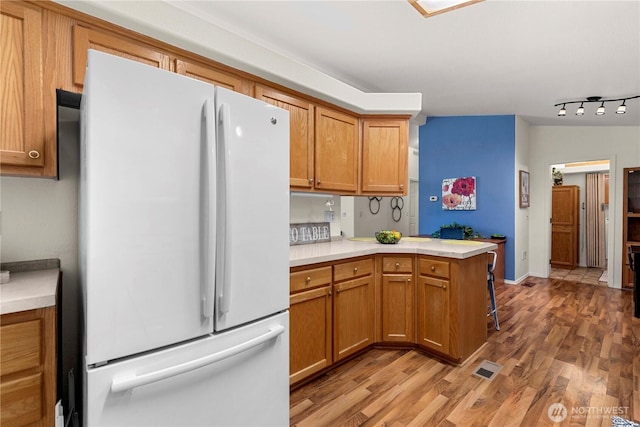 kitchen with light countertops, light wood-style floors, brown cabinets, and freestanding refrigerator