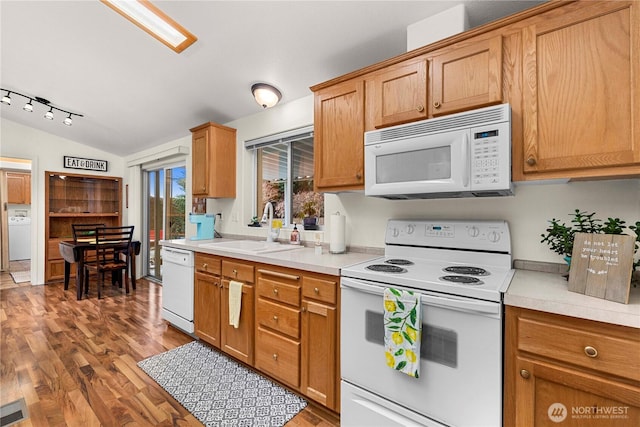 kitchen featuring white appliances, wood finished floors, washer / dryer, a sink, and vaulted ceiling