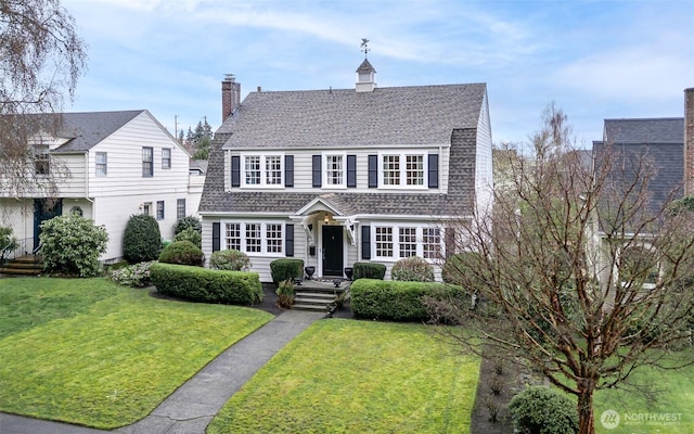 view of front facade with a front lawn, a gambrel roof, roof with shingles, and a chimney