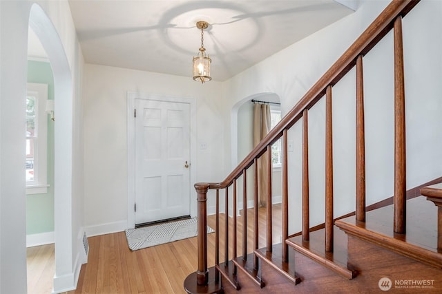 entryway featuring stairs, wood finished floors, arched walkways, and baseboards