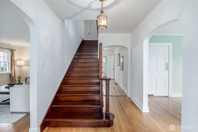 stairway featuring arched walkways, baseboards, and wood finished floors