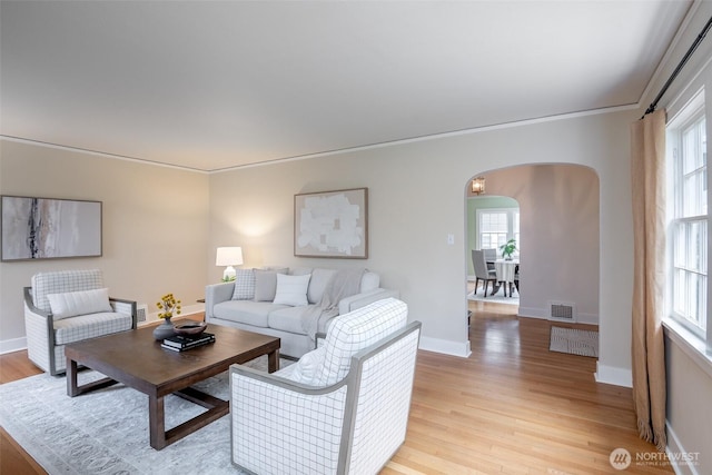 living area with arched walkways, visible vents, light wood-style flooring, and baseboards