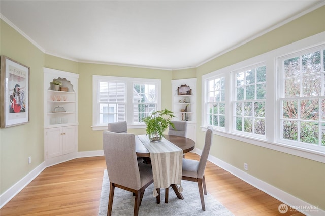 dining room featuring built in shelves, baseboards, ornamental molding, and light wood finished floors