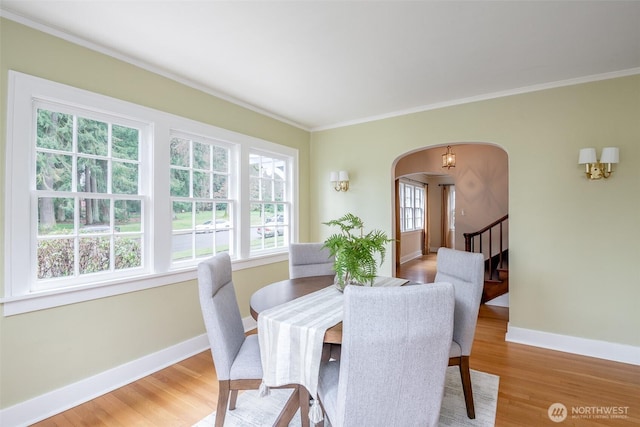 dining area with arched walkways, crown molding, light wood-type flooring, and baseboards