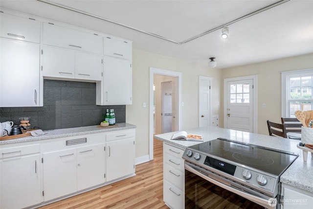 kitchen with light wood-type flooring, track lighting, tasteful backsplash, stainless steel range with electric cooktop, and white cabinets