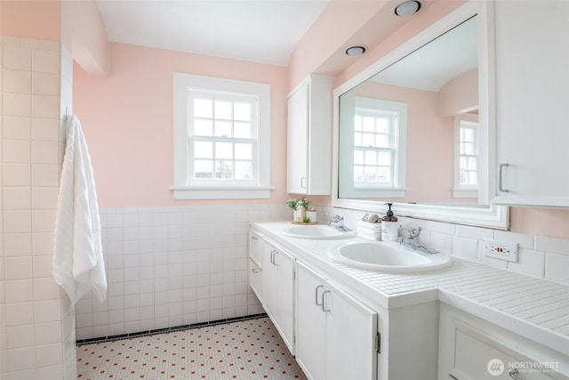 bathroom featuring a sink, a wainscoted wall, tile walls, and double vanity