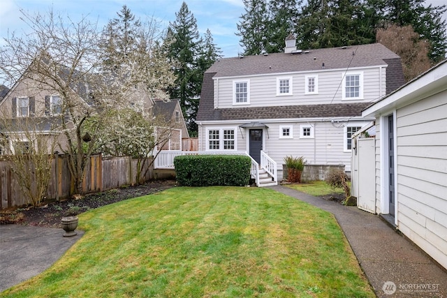 rear view of house with fence, entry steps, roof with shingles, a chimney, and a yard