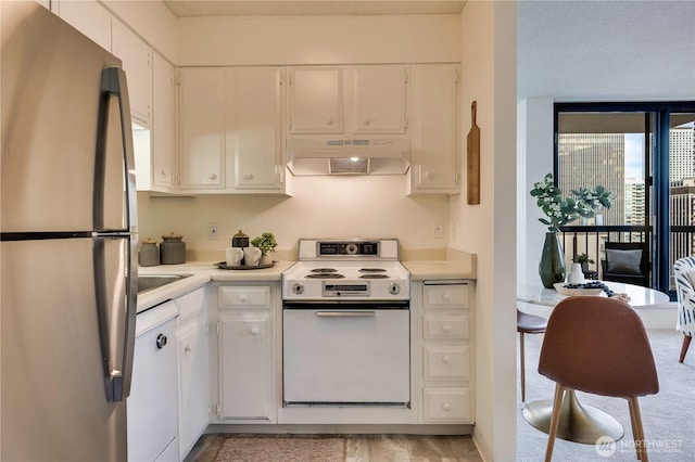 kitchen with under cabinet range hood, white appliances, white cabinetry, and light countertops