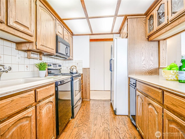 kitchen featuring light countertops, decorative backsplash, glass insert cabinets, light wood-type flooring, and black appliances