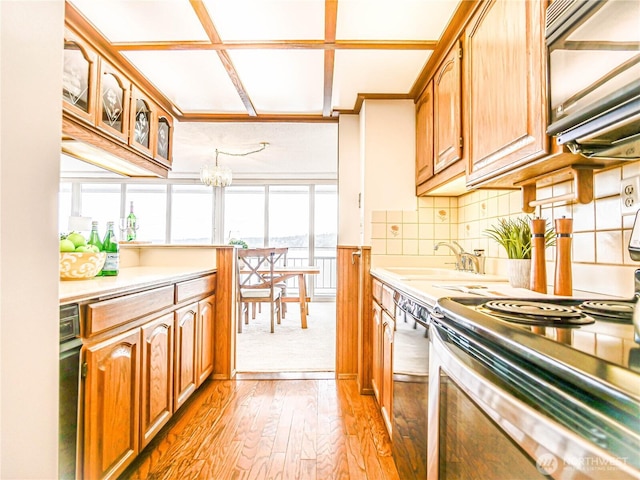 kitchen featuring light wood finished floors, light countertops, backsplash, dishwasher, and stainless steel electric range oven