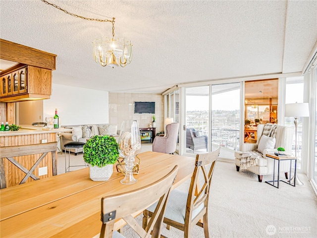 dining room featuring a chandelier, light carpet, a textured ceiling, and a wall of windows