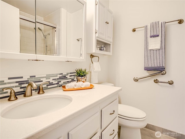 bathroom with toilet, vanity, baseboards, a tile shower, and backsplash