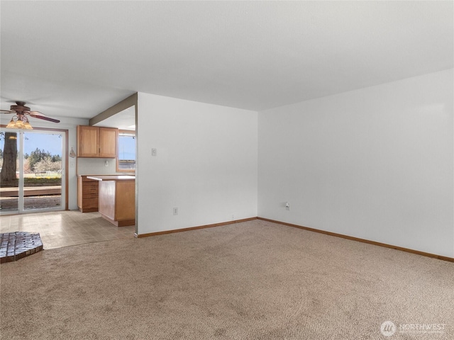 unfurnished living room featuring a ceiling fan, light colored carpet, and baseboards